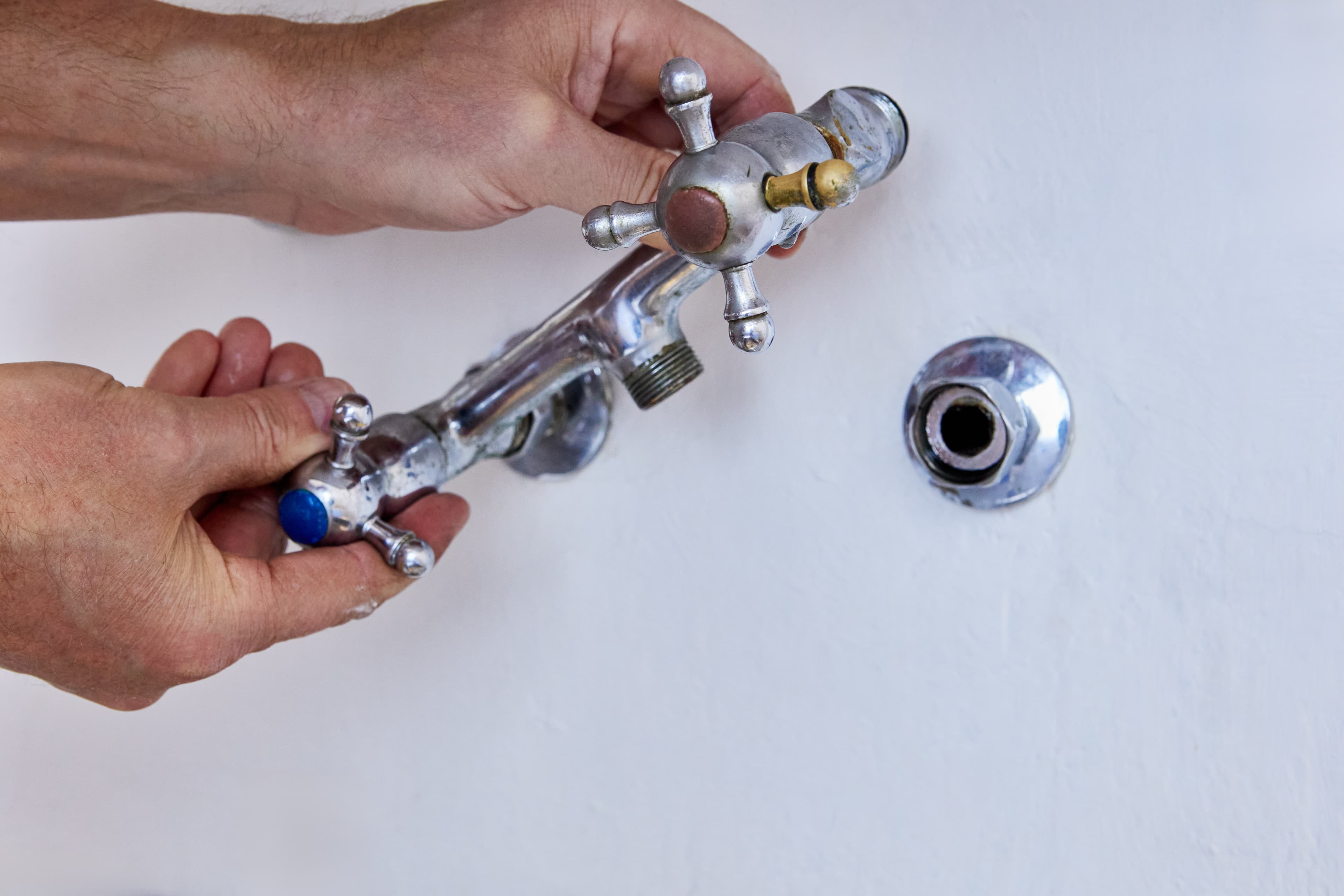 Сантехник снимает старый смеситель со стены перед заменой